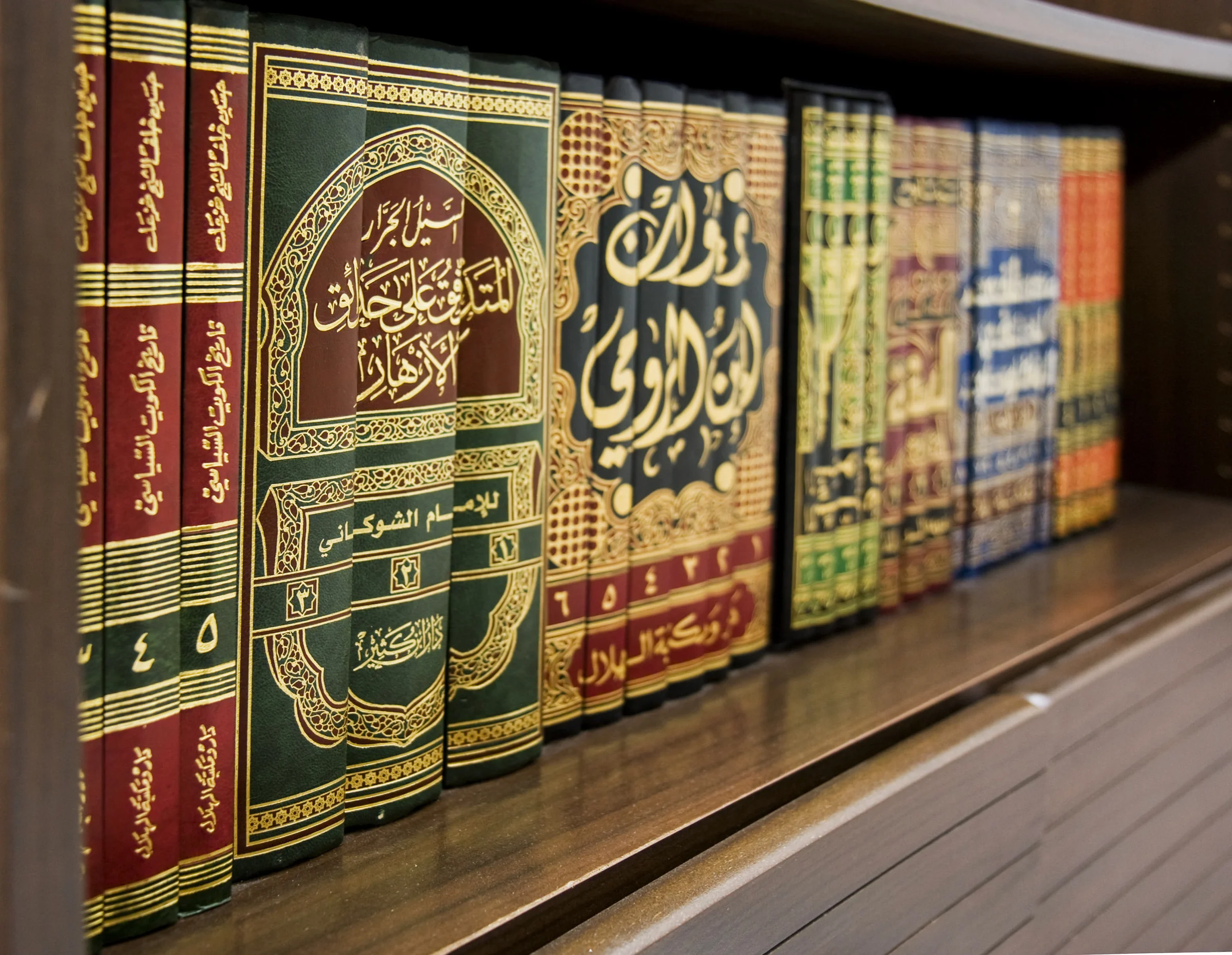 Rows of ornate Arabic-language books on a wooden library shelf